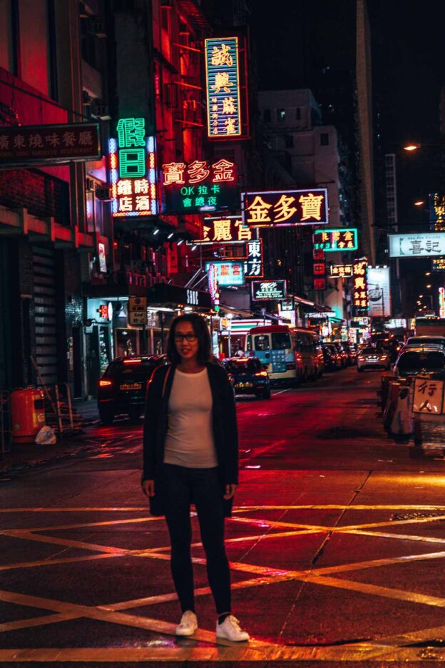A girl posts at a pedestrian crossing at night illuminated by neon lights in the Mong Kok neighbourhood, Hong Kong
