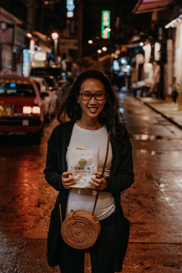 A girl smiles broadly holding a fresh egg waffle in the streets of Mong Kok, Hong Kong