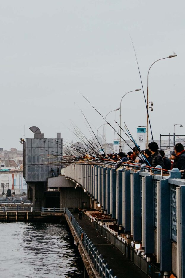 Hundreds of men stand atop Galata Bridge with fishing rods, casting their lines into the Bosphorus Strait. Istanbul, Türkiye