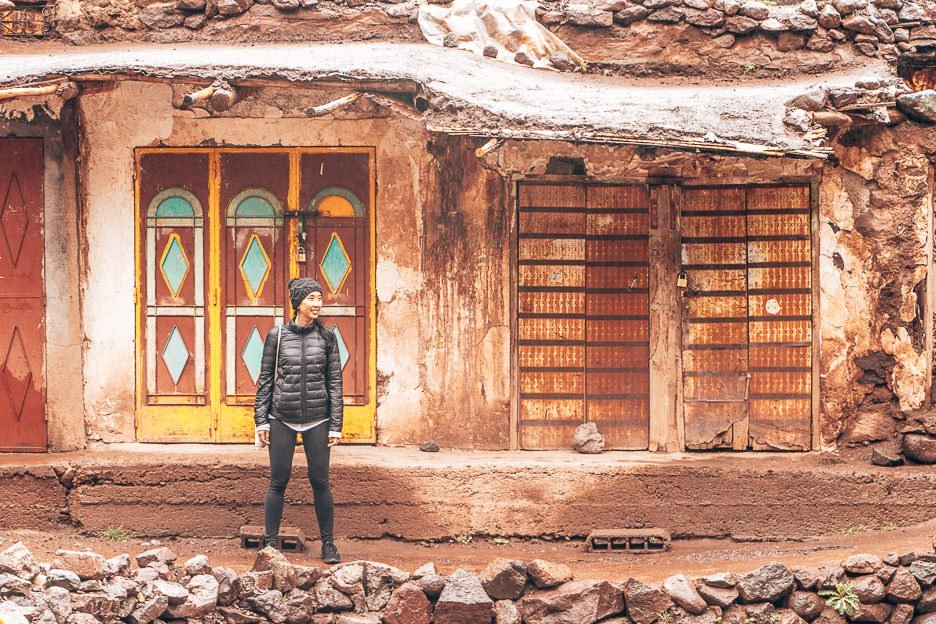 Jasmine stands in front a hut with rusted doors in the Atlas Mountains, Morocco
