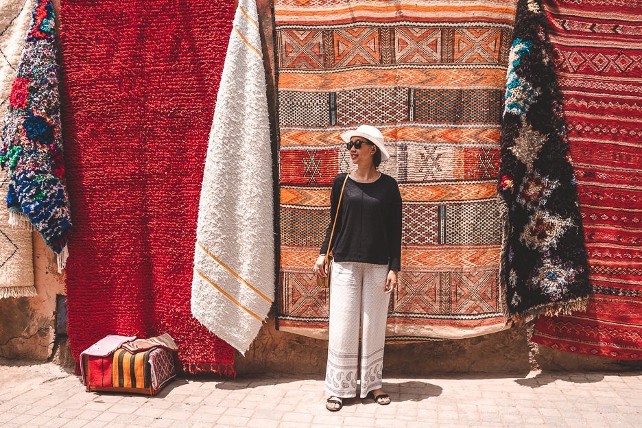 Jasmine stands in front of colourful woven rugs in Marrakech medina, Morocco