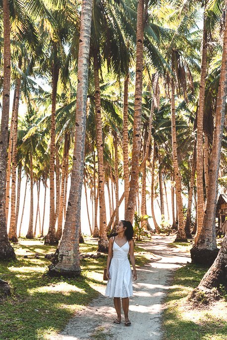 A lady in a white dress walks along a path lined with palm trees, Siargao