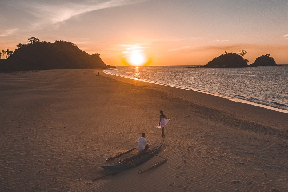 A couple next to a beached boat watching the sunset on Nacpan Beach, El Nido