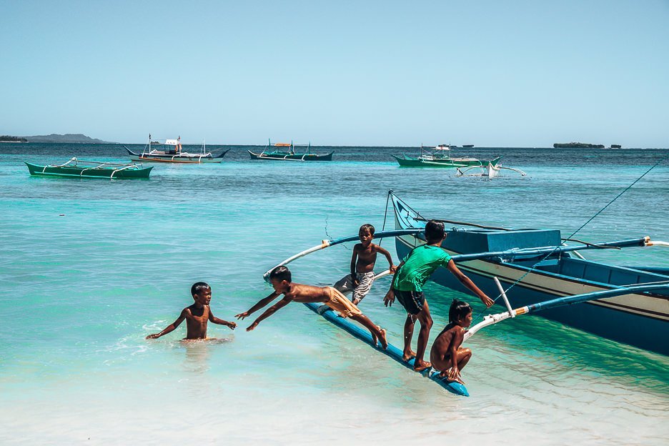 Young children jump off a traditional Filipino boat into the water, Siargao
