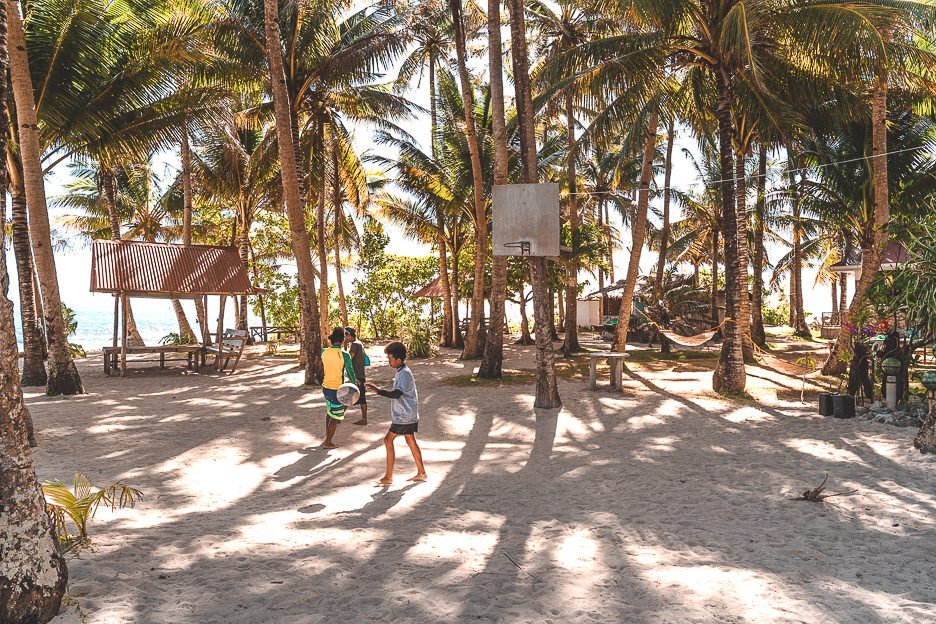 Three local boys playing basketball on a sandy court on Guyum Island, Siargao