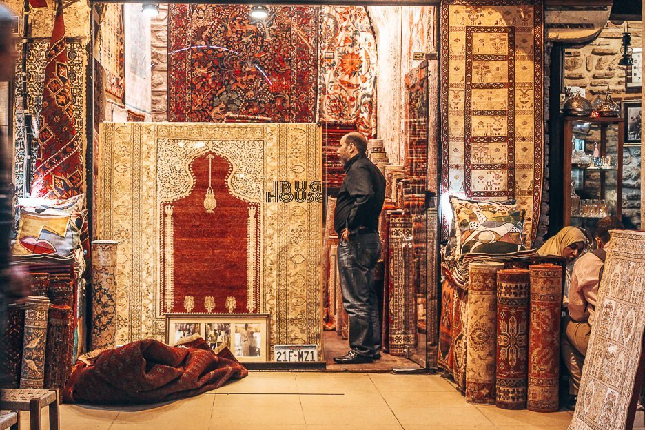 A man stands at the entrance of his rug shop inside the Grand Bazaar - Istanbul City Guide, Turkey