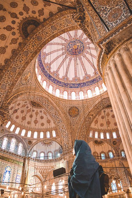A woman covers her head with a shawl and looks up at the immaculate detail inside The Blue Mosque, Istanbul
