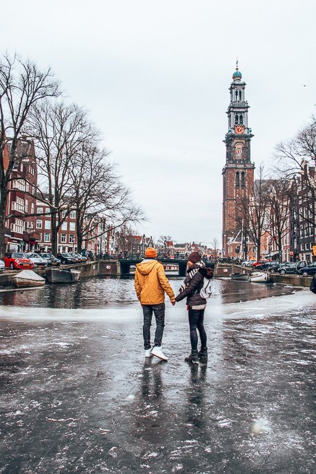 A couple stand on a frozen canal in front of Westerkerk, Amsterdam