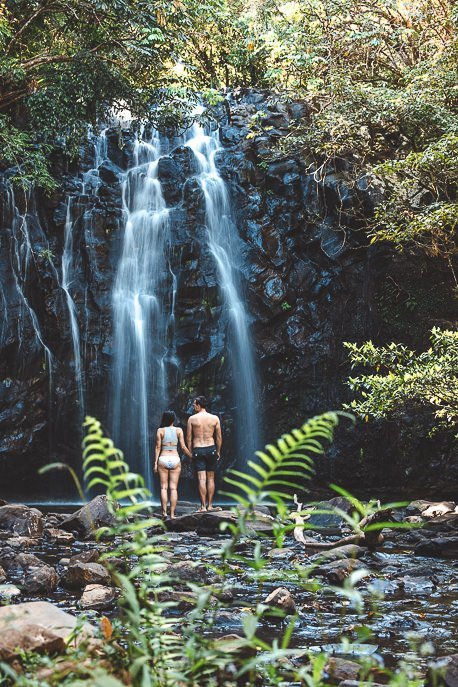 A couple stand hand in hand in front of Ellinjaa Falls in Wooroonooran National park, Queensland