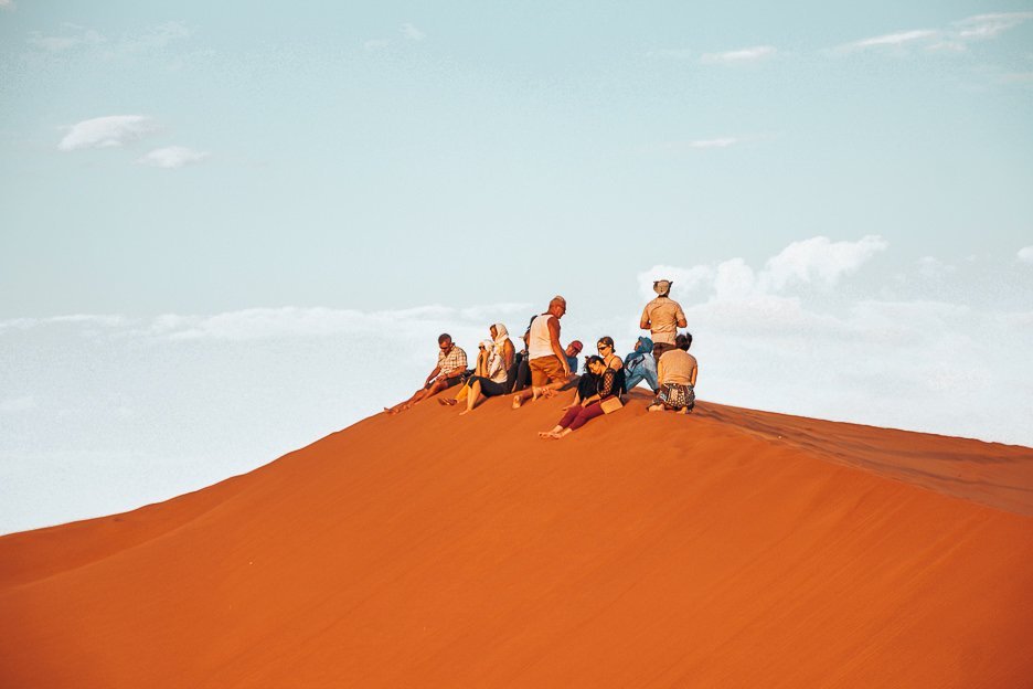 A group sit on the peak of a sand dune in the Sahara Desert, Morocco