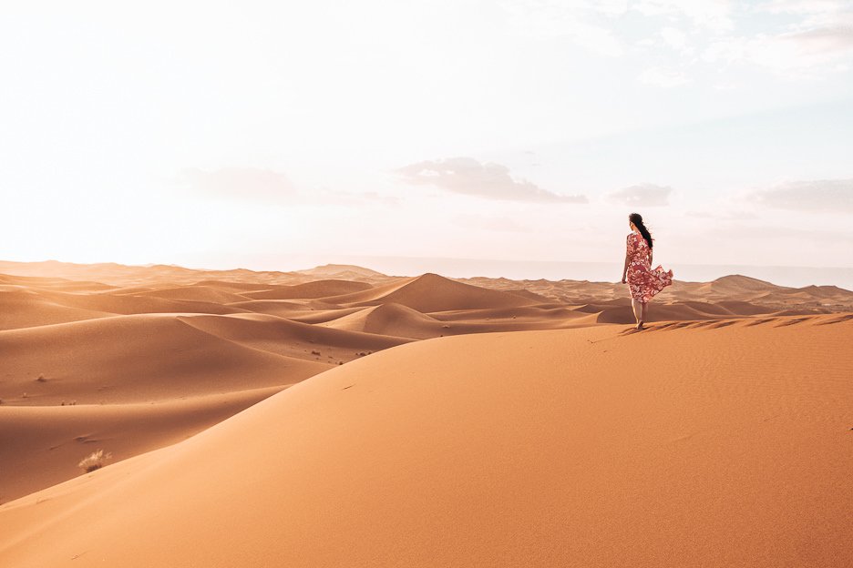 Camping Under The Stars A Night In The Sahara Desert 1 L A woman in a red dress stands on a sand dune looking out into the distance in the Sahara Desert, Morocco