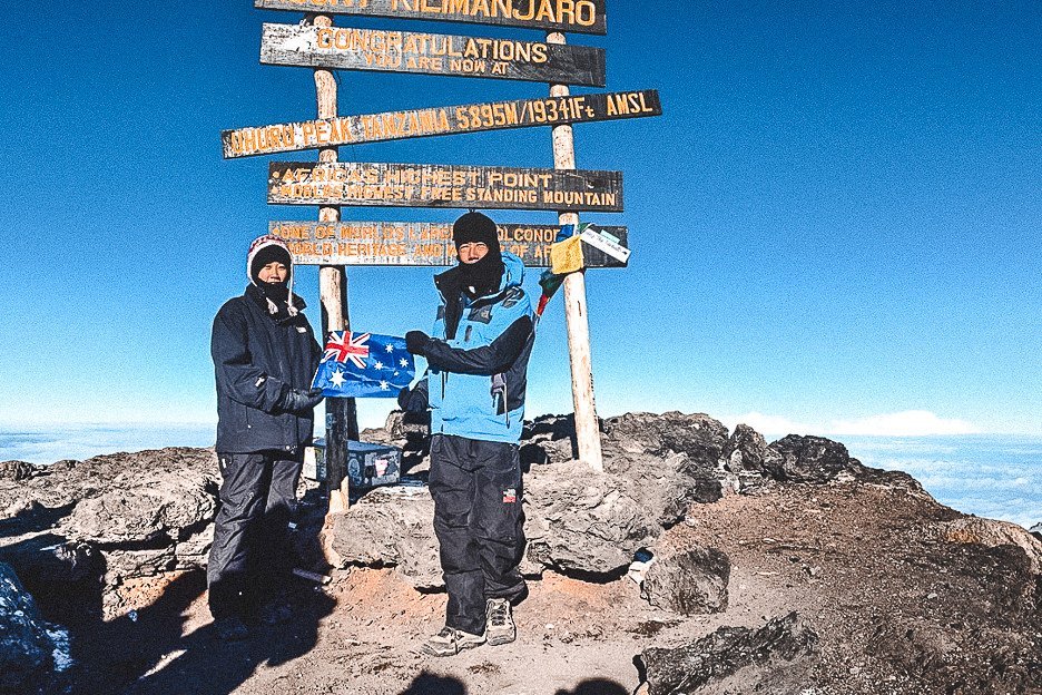 Jasmine standing with her dad holding an Australian flag at the top of Mt Kilimanjaro