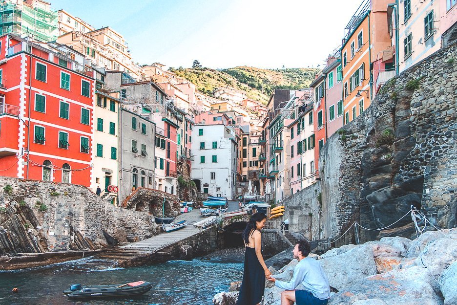 A couple sit on the rocks in the harbour of RIomagiorre, Cinque Terre, Italy
