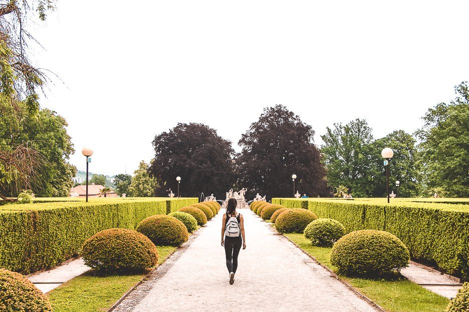 A girl with a white backback walks down a path with perfectly trimmed hedges, Zámecký park, Český Krumlov