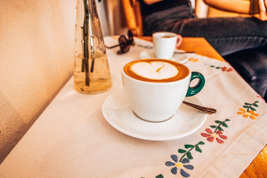A flat white coffee on a floral embroided tablecloth at Ideal Coffee, Český Krumlov
