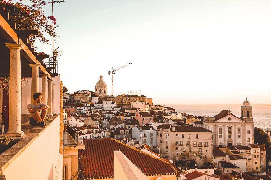Bevan sits on a miradouro ledge watching sunrise over Lisbon, Portugal