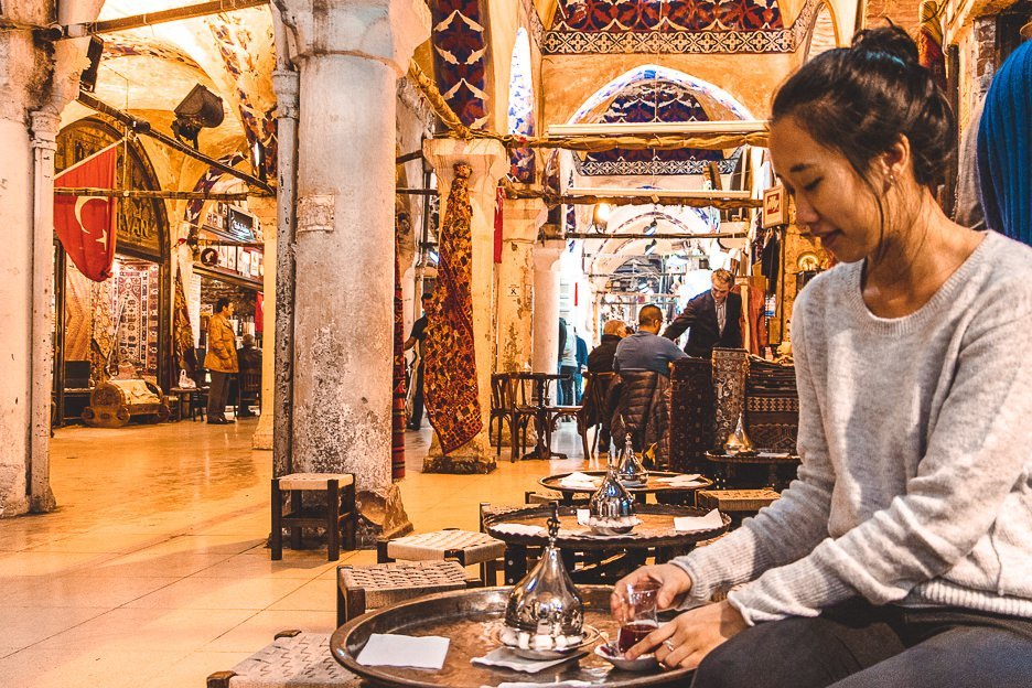 A girl sits on a low stool sipping cay in the Grand Bazaar, Istanbul
