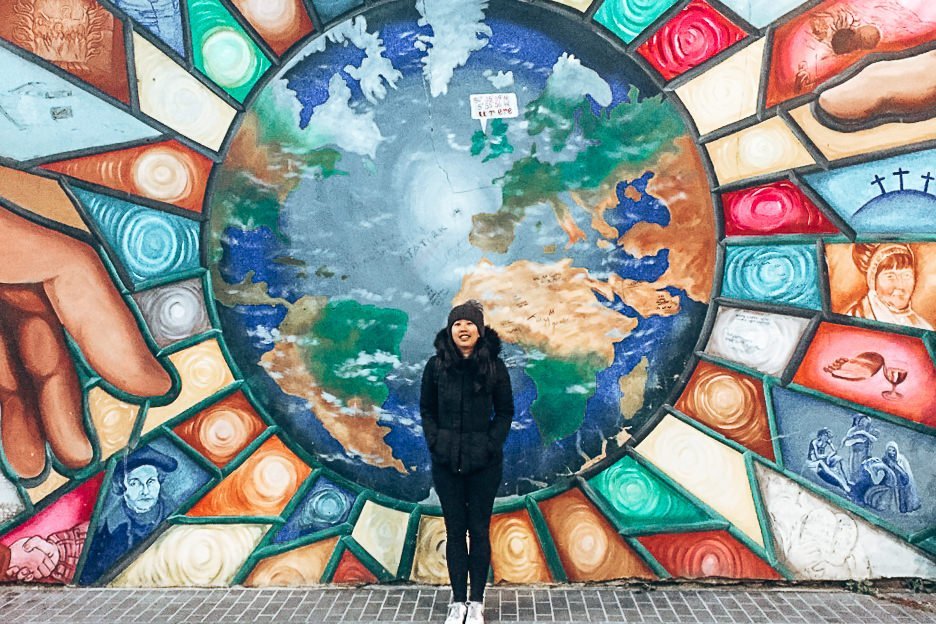 Jasmine stands in front of a Peace mural in Belfast, Northern Ireland