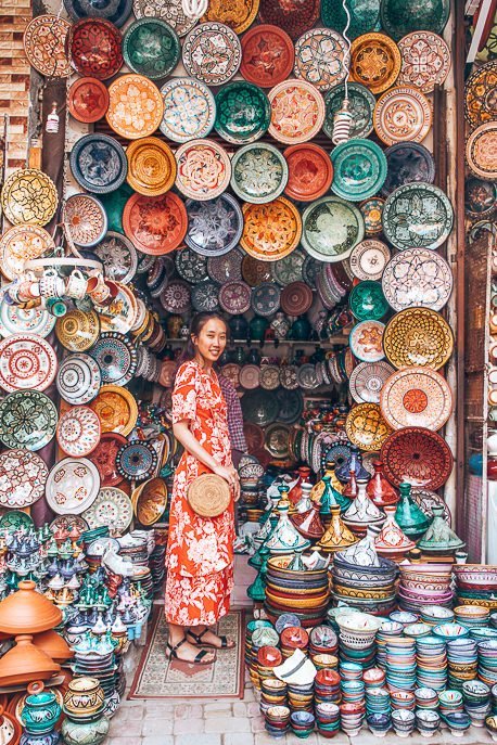 A woman in a red dress stands at the entrance of a ceramics shop in the souks of Marrakech, Morocco