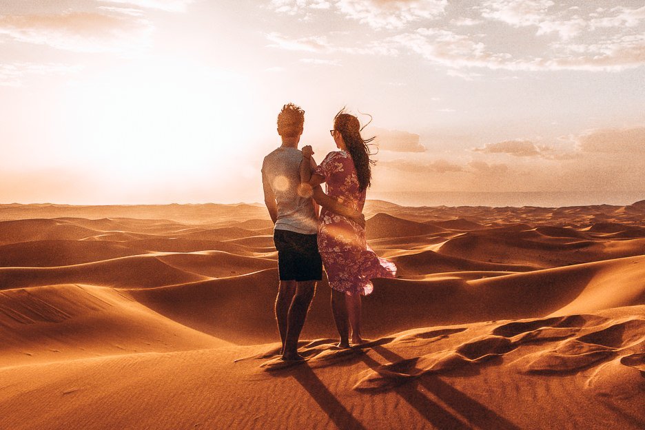 A couple stand on the edge of a sand dune in the Sahara Desert during sunset, Morocco