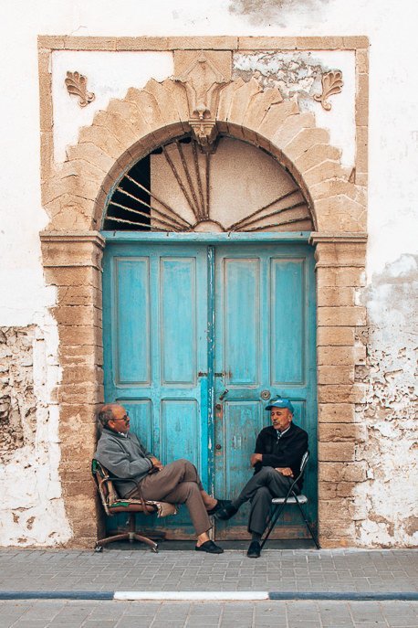 Two men sit outside blue door in Essaouira Morocco
