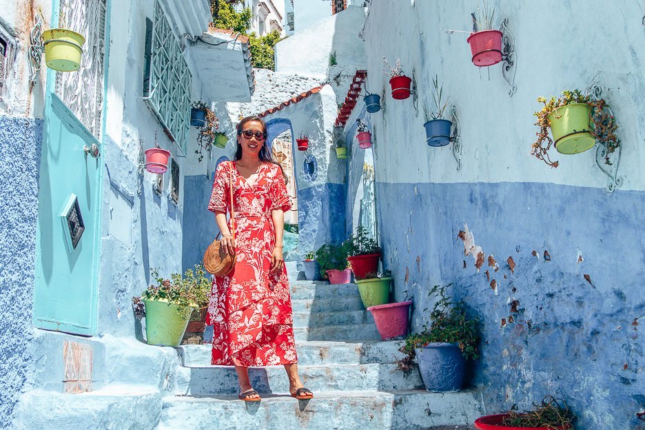 A woman in a red dress poses for a photo on the blue steps of Chefchaouen, Morocco