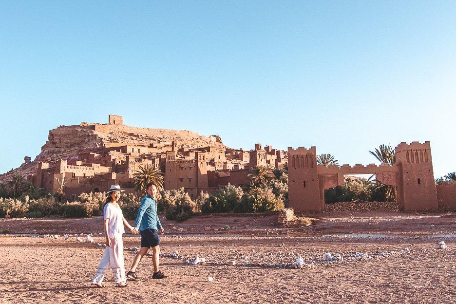 A couple walk hand in hand in front of the ancient kasbah of Ait Benhaddou, Morocco