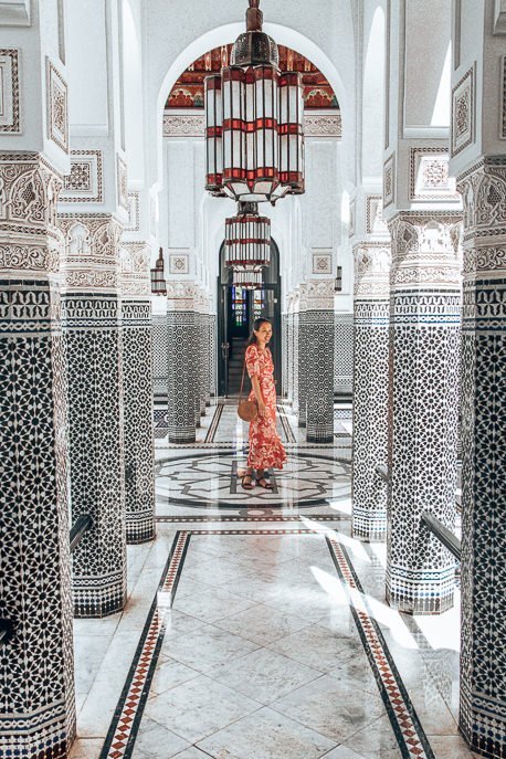 A woman in a red dress twirls in a black and white mosaic atrium in La Mamounia, Marrakech, Morocco