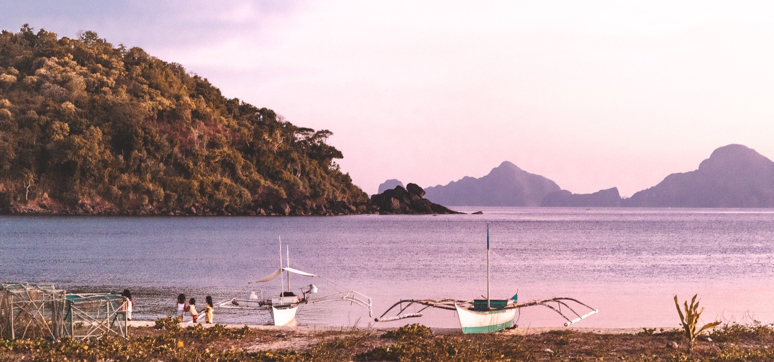 Boats sit on the shore of Nacpan Beach at sunset, El Nido, The Philippines