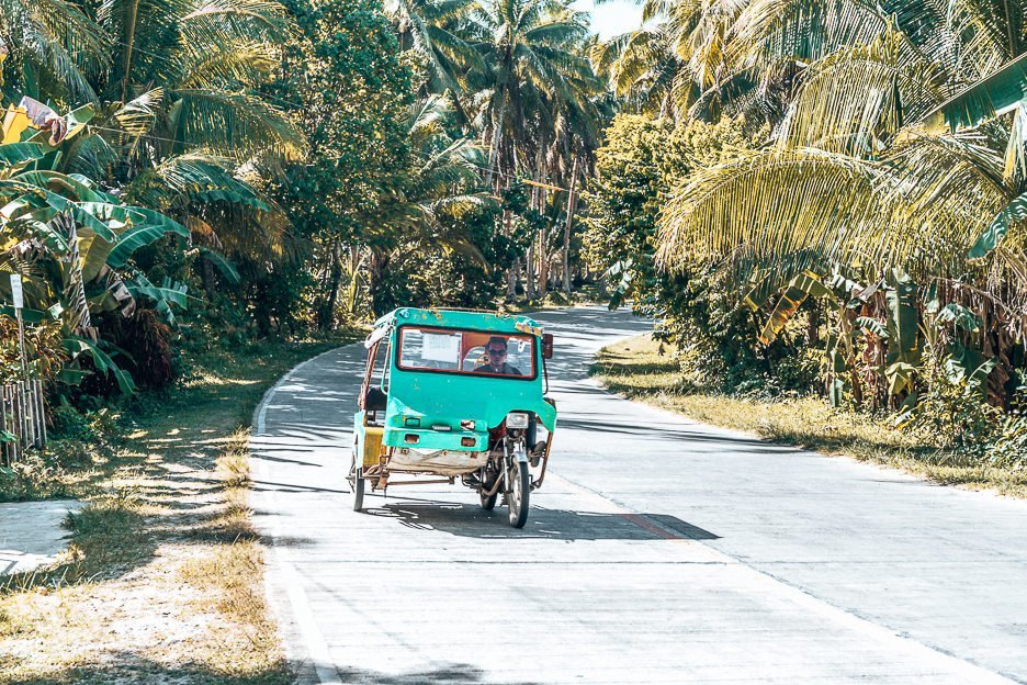 A green tricycle trundles along Tourism Road, Siargao
