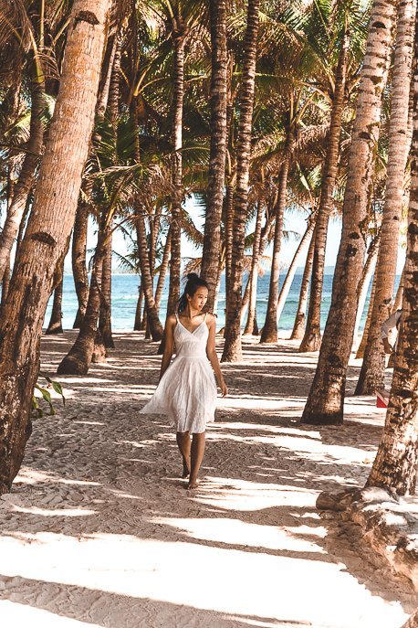 A girl in a white dress walks through the palm trees at Cloud Nine, Siargao