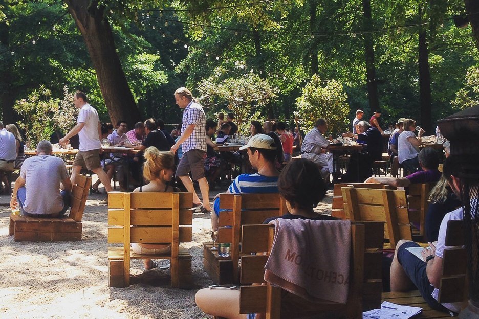 People sit on wooden seats drinking beer in the beergarden at Cafe Am Neuen See, Berlin