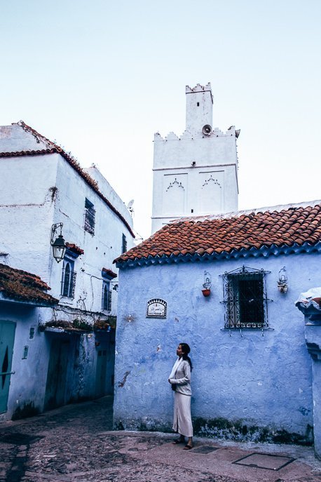 A woman wears a white dress standing in front a blue building in Chefchaouen, Morocco