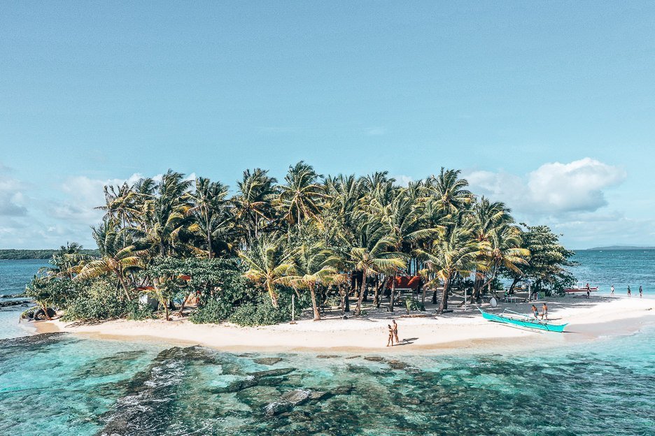 The Ultimate Beach Packing List 1 L Aerial view of Guyam Island, a couple walk hand in hand on the beach next to a beached blue boat
