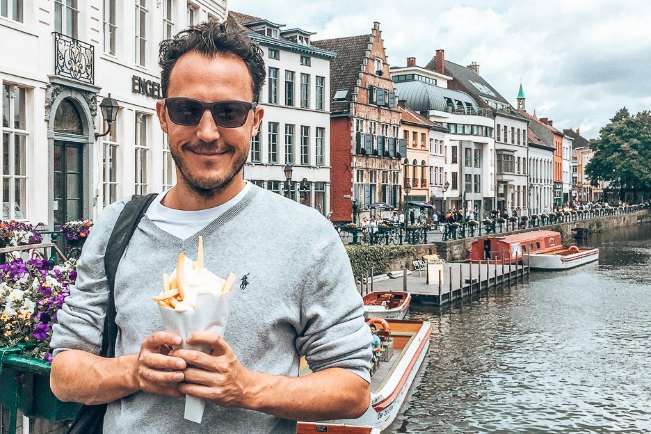 The Undiscovered Flemish Jewel A Day Trip To Ghent 6 L Bevan holding fries in front of one of the canals in Ghent, Belgium
