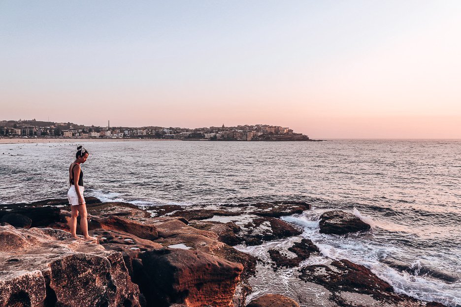 A woman stands on the rocks in Bondi Beach during sunrise