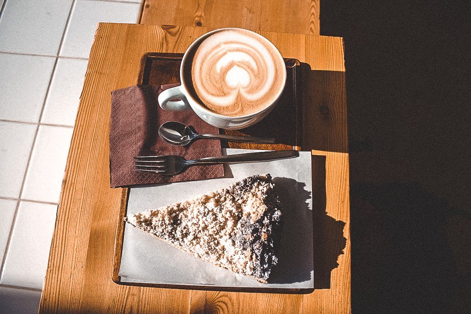 A flat white and slice of pie on a table in the sunshine at EMA Espresso Bar, Prague, Czech Republic