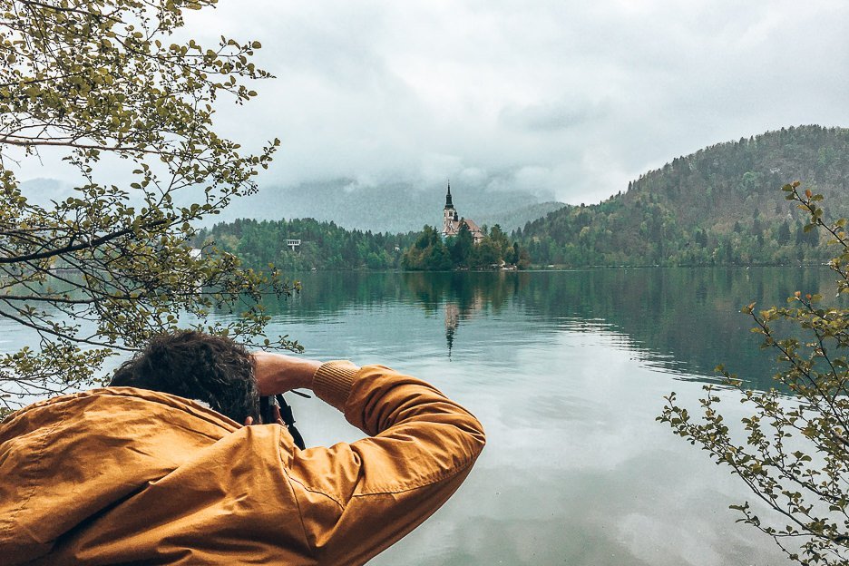 A man in a yellow jacket snaps a photo of Bled Castle on Bled Lake | Photography Camera Bag