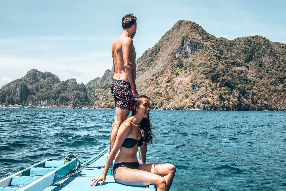 A couple perch on the end of a Filipino boat during a day cruise in El Nido, The Philippines