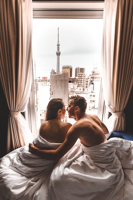 A man and a woman under white duvets looking out at Tokyo Skytree - The Gate Hotel Kaminarimon by HULIC