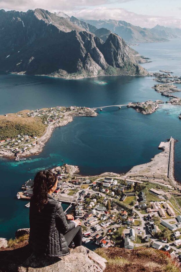 A girl dressed in black perches on a rock atop Reinebringen whilst looking out over the town of Reine. Lofoten Islands, Norway