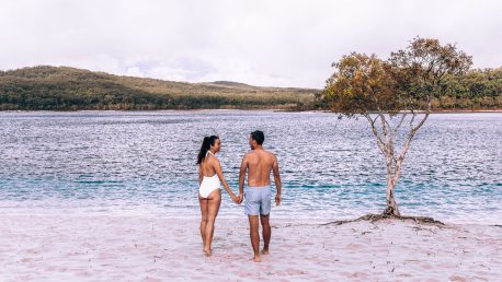 A couple hold hands on the sand at the edge of Lake McKenzie, Fraser Island