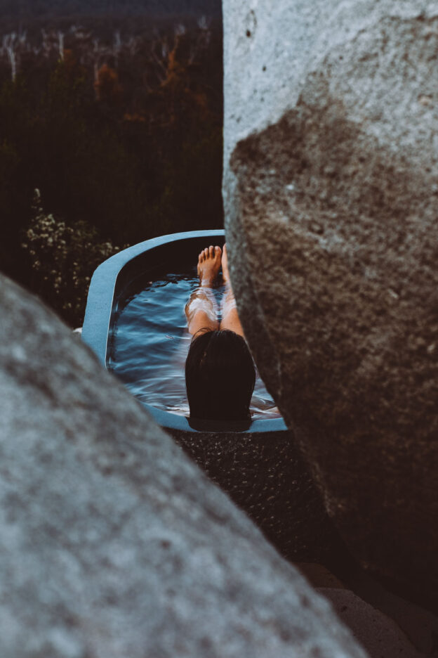 Peeking through the boulders, a woman enjoys the hot water of the outdoor bath at The Keep. Tasmania, Australia