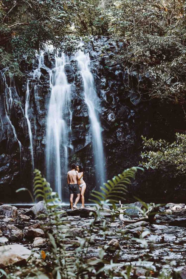 A long exposure shot of a couple standing in front of Ellinjaa Waterfall in tropical north Queensland, Australia