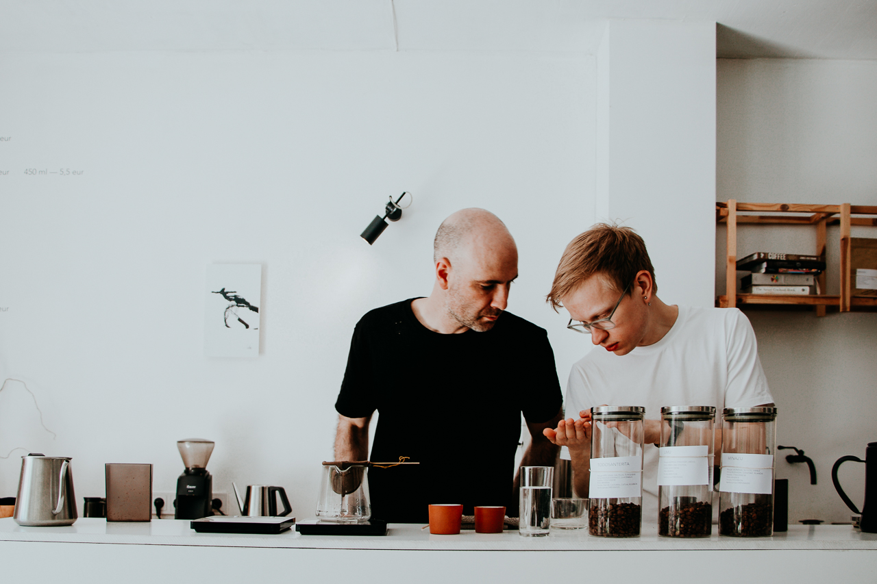 Two baristas examine coffee beans at the counter of Crooked Nose & Coffee Stories cafe. Vilnius, Lithuania